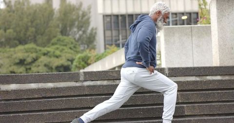 Mature african american man performing lunge on urban steps wearing navy hoodie and gray sweatpants
