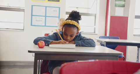 Young Student Writing at Desk with Apple in Classroom