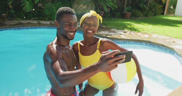 Happy african american couple standing in swimming pool taking selfie and smiling in sunny garden. staying at home in isolation during quarantine lockdown.