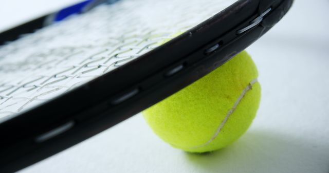 This image shows a close-up of a tennis racket gently resting atop a tennis ball against a clean white background. Ideal for use in advertising sports goods, promoting active lifestyle, or illustrating tennis-related content in articles and blogs.