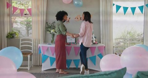 Holding hands celebrating couple at pastel baby shower with bunting, balloons and cake