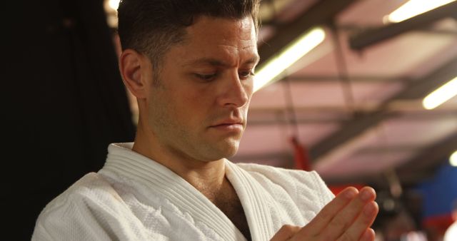 Martial artist wearing white gi focusing and meditating before training session. Ideal image for articles on martial arts discipline, mindfulness in martial arts, or promoting dojos and martial arts schools. Can be used in blog posts, training manuals, or motivational content.