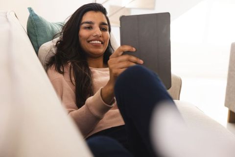 Smiling woman using tablet while relaxing on sofa at home