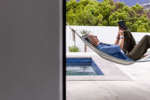 Mature woman relaxing in hammock by pool reading tablet on modern terrace