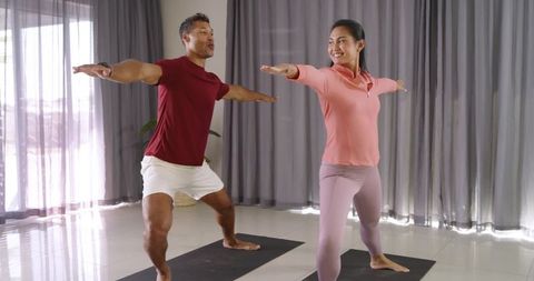 Man and Asian Woman Practicing Warrior II Yoga in Sunlit Minimal Studio