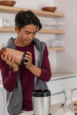 Young asian man shaking blender cup making chocolate smoothie in modern minimal kitchen