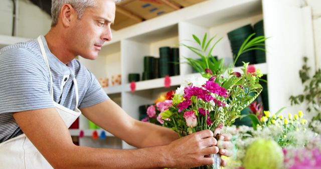 Male florist carefully arranging a colorful floral bouquet in a florist shop. Suitable for themes of small business, professional florist, creative crafts, and the art of floral arrangement. Ideal for use in marketing material for florists, flower industries, and creative professions.