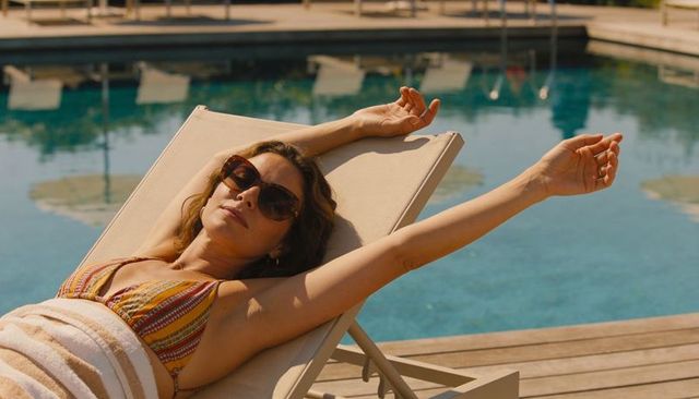 Sunbathing woman stretching on poolside lounger in striped bikini and sunglasses
