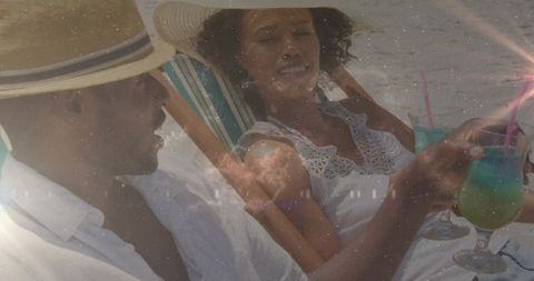 Couple lounging on beach chairs sipping teal cocktails wearing straw hats and white linen