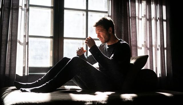 Backlit man sitting on daybed in dark loungewear, contemplative light with dust motes