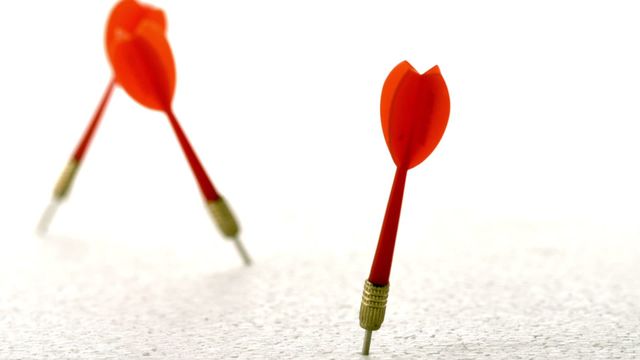 Two red darts piercing a white surface are shown close up in slow motion. Perfect for conveying themes of precision, accuracy, and focus in business presentations, motivational posters, or educational materials.