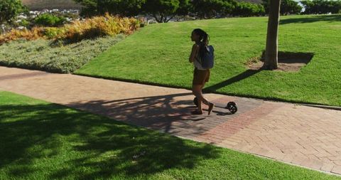 Woman Walking with Electric Scooter on Park Path in Bright Summer Day