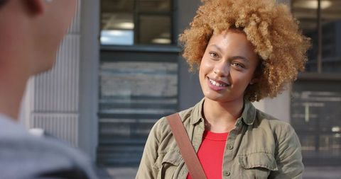 Smiling young woman chatting with friend on sunny urban sidewalk, casual lifestyle