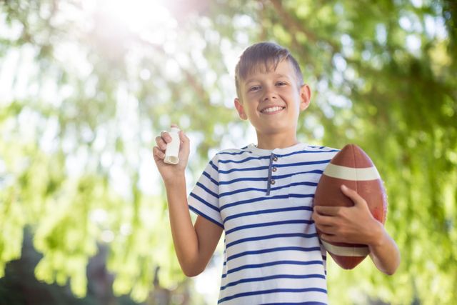 Boy holding asthma inhaler and a rugby ball on a sunny day