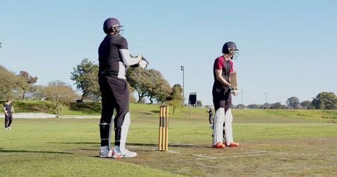 Teammates practicing cricket outdoors on sunny day