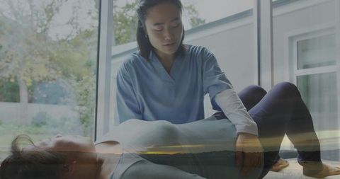 Female caregiver supporting patient hip during physical therapy by window