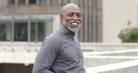 Senior african american man smiling standing on urban concrete terrace wearing grey zip top