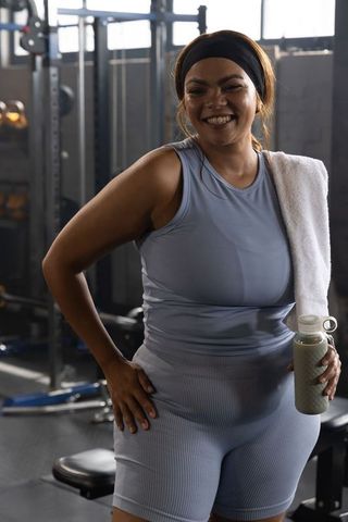 Smiling african american woman training in gym holding water bottle and towel