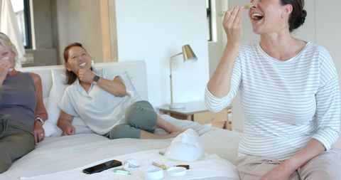 Laughing women lounging on bed during skincare night sharing masks and selfcare ritual