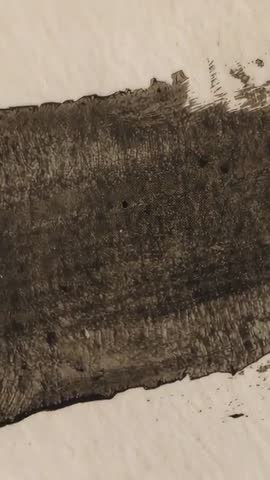 Vertical macro footage revealing wide dark brushstroke on off-white textured paper for close study