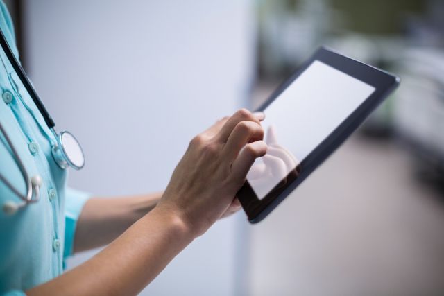 Female doctor using digital tablet in hospital corridor. Ideal for illustrating modern healthcare, medical technology, and professional medical staff. Suitable for use in healthcare websites, medical blogs, and technology in medicine articles.