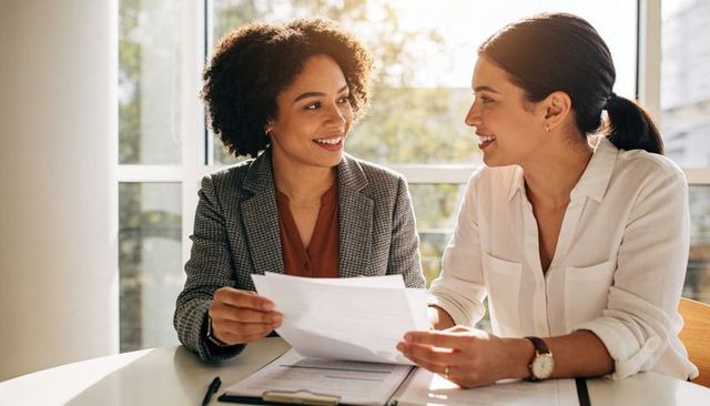 Smiling businesswomen reviewing documents and collaborating at bright modern office table