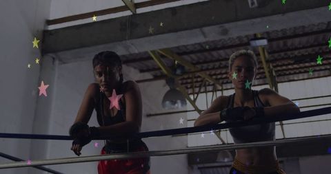 Two boxers leaning on ring ropes resting between rounds in gritty industrial gym