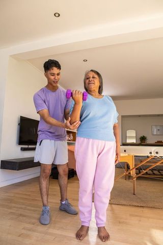 Supportive Fitness Trainer Assisting Senior Woman with Dumbbell Workout