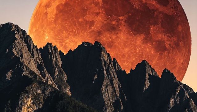Jagged mountain ridge framing giant blood moon over twilight peaks