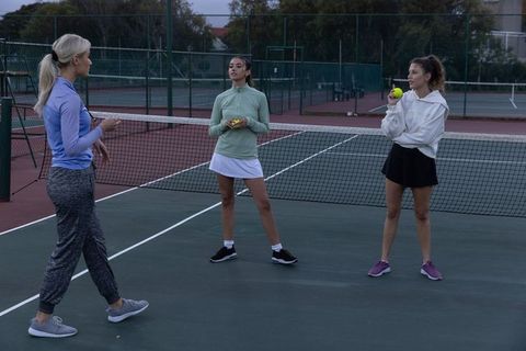 Female coach instructing two tennis players during evening practice on outdoor court