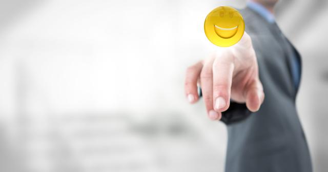 Businessman wearing suit pointing finger at floating smiling emoji in modern, blurred office environment. Represents digital communication, positive interaction and innovation in corporate settings. Suitable for tech-driven business websites, presentations on digital transformation, positive workplace illustrations, and professional communication themes.
