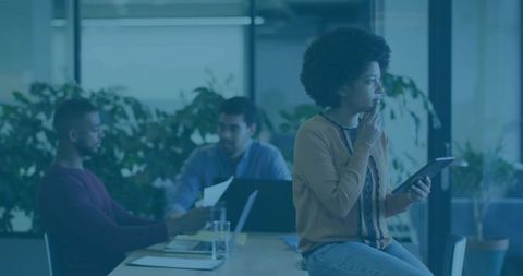 Pensive professional holding tablet while collaborating with team in modern office meeting