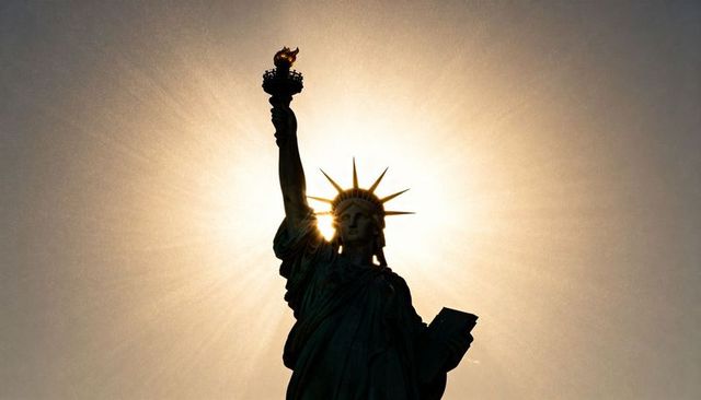 Statue of liberty silhouette with radiant halo and torch flame in golden backlight