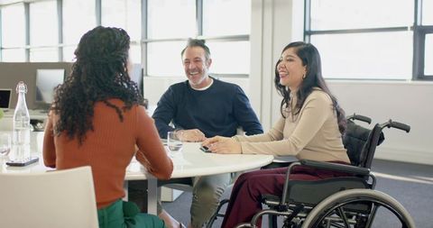 Inclusive team collaborating around round table with wheelchair in modern office