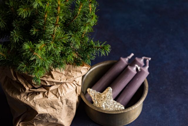 Christmas tree wrapped in rustic brown paper bag placed beside a wooden bowl containing purple candles and a glittery star decor on dark table. Perfect for holiday-themed promotions, Christmas crafts tutorials, holiday decor inspirations, and seasonal blog posts.