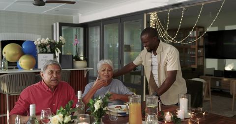 Multigenerational family celebrating cozy candlelit dinner with balloons, flowers, wine
