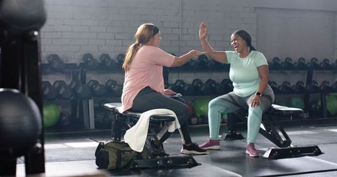 Women high-fiving after workout while sitting on gym benches