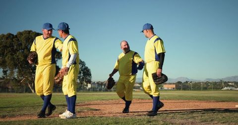 Mature baseball teammates walking and laughing on pitcher's mound wearing yellow jerseys