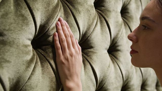 Woman touching green velvet tufted headboard closeup tactile luxury bedroom texture