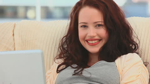 Smiling Woman Relaxing with Laptop on Sofa