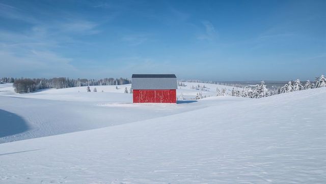 Red Barn Standing Alone on Snowy Hill under Clear Blue Sky Minimalist Winter Landscape