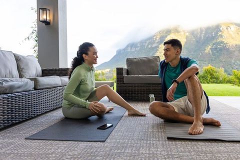 Asian couple practicing yoga and chatting on covered patio with mountain view