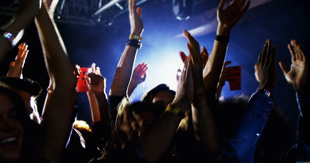 Energetic crowd enjoying a concert at night, with copy space. Raised hands capture the excitement of live music in an indoor setting.