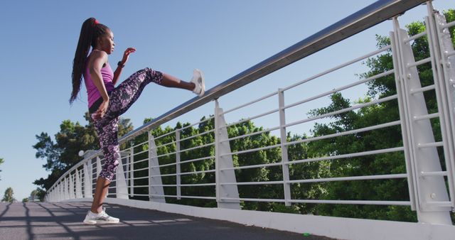African american woman stretching her leg on the railing of the city bridge. fitness sports and active lifestyle concept