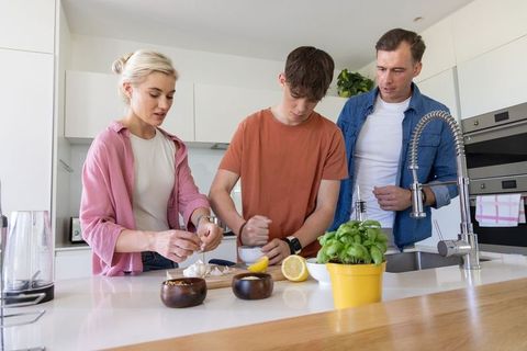 Family cooking together in bright modern kitchen preparing fresh meal with teen