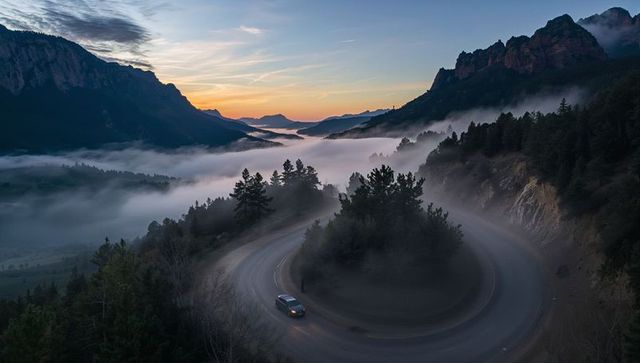 SUV navigating foggy mountain hairpin turn at sunrise, winding alpine valley view