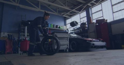 Female mechanic changing tire in industrial garage with sports car and toolbox