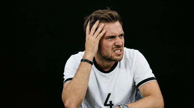 Male athlete grimacing while clutching head on sideline bench wearing jersey number 4