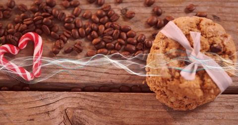 Warm rustic flatlay featuring oatmeal cookie tied with bow, coffee beans and candy cane heart with d