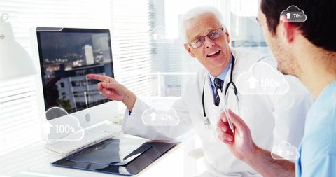 Senior doctor pointing at monitor while trainee reviewing cloud-based patient data